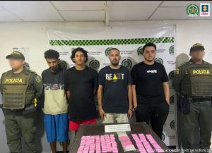 En la imagen están cuatro hombres de pie custodiado por dos agentes de la Policía Nacional. Delante de ellos aparece una mesa donde se encuentra el estupefaciente incautado.