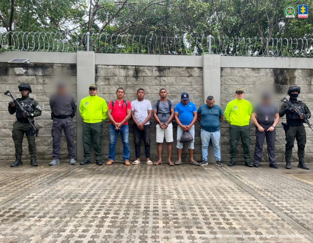 En la fotografía están los procesados de pie con los brazos hacia adelante esposados. Se encuentran acompañados de uniformados del CTI y de la Policía Nacional.