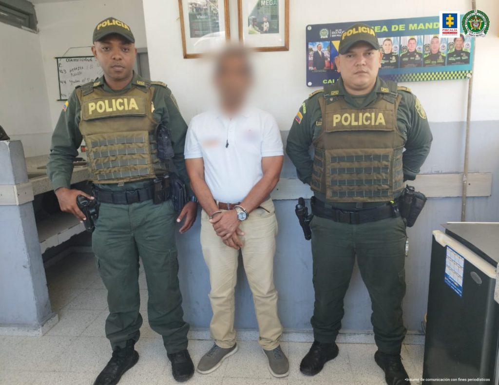 En la imagen se observa a un hombre con camiseta blanca y pantalón beis, custodiado por dos agentes de la Policía Nacional.