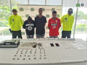 En la fotografía aparecen una mujer y dos hombres custodiados por dos agentes de la Policía Nacional. Detrás de ellos está un pendón de esa institución y delante se encuentra una mesa con bolsas de cocaína, celulares y marihuana que incautaron.
