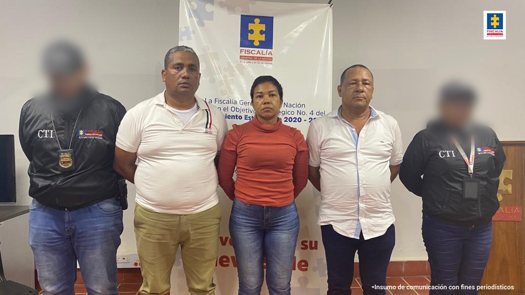 En la imagen se observa a dos hombres y a una mujer custodiados por uniformados del CTI, delante de un pendón que dice Fiscalía General.