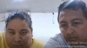 En la fotografía están un hombre y una mujer de contexturas gruesas, morenos, ambos de cabellos negros, ella se encuentra vestida con una camiseta amarilla y el con una camiseta gris. Están sentados al interior de una oficina asistiendo virtualmente a la audiencia en la que se les proceso.
