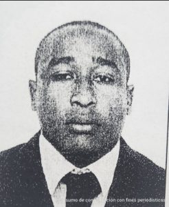 En la fotografía a blanco y negro está el rostro de un hombre moreno, con pelo muy corto, ojos pequeños, nariz y boca grande, vestido con saco y corbata.