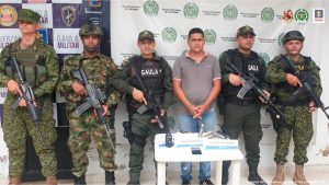 En la fotografía se observa a un hombre vestido de camiseta gris con jean custodiado por uniformados del Ejército y la Armada Nacional.