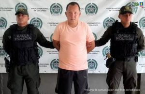 En la foto está un hombre trigueño, de pie, de frente, con los brazos atrás esposados, de contextura gruesa, cabellos cortos negros, está vestido con una camiseta rosada y una bermuda negra. A su lado están dos uniformados de la Policía Nacional. 