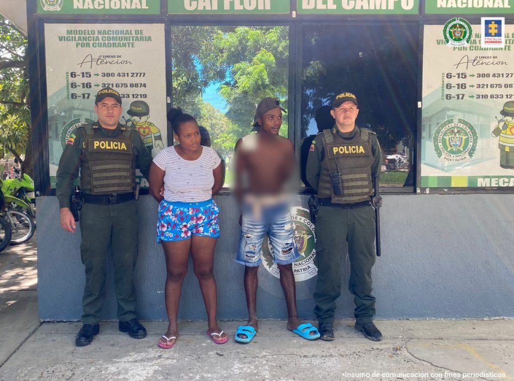 En la fotografía se observan a un hombre y a una mujer de tez morena, custodiados por dos agentes de la Policía Nacional en una estación de Policía.