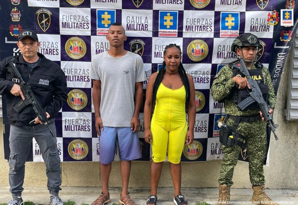 En la fotografía aparecen un hombre moreno, vestido de camiseta gris, con bermuda azul y una mujer morena con enterizo amarillo, custodiado por un servidor del CTI de la Fiscalía y un uniformado del Ejército Nacional.