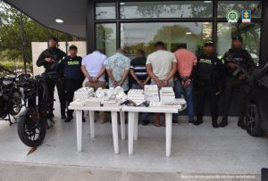 En la fotografía están cinco hombres de espalda, con los brazos esposados, custodiado por cuatro agentes de la Policía Nacional armados. Delante de ellos hay una mesa blanca con las joyas y las armas incautadas.