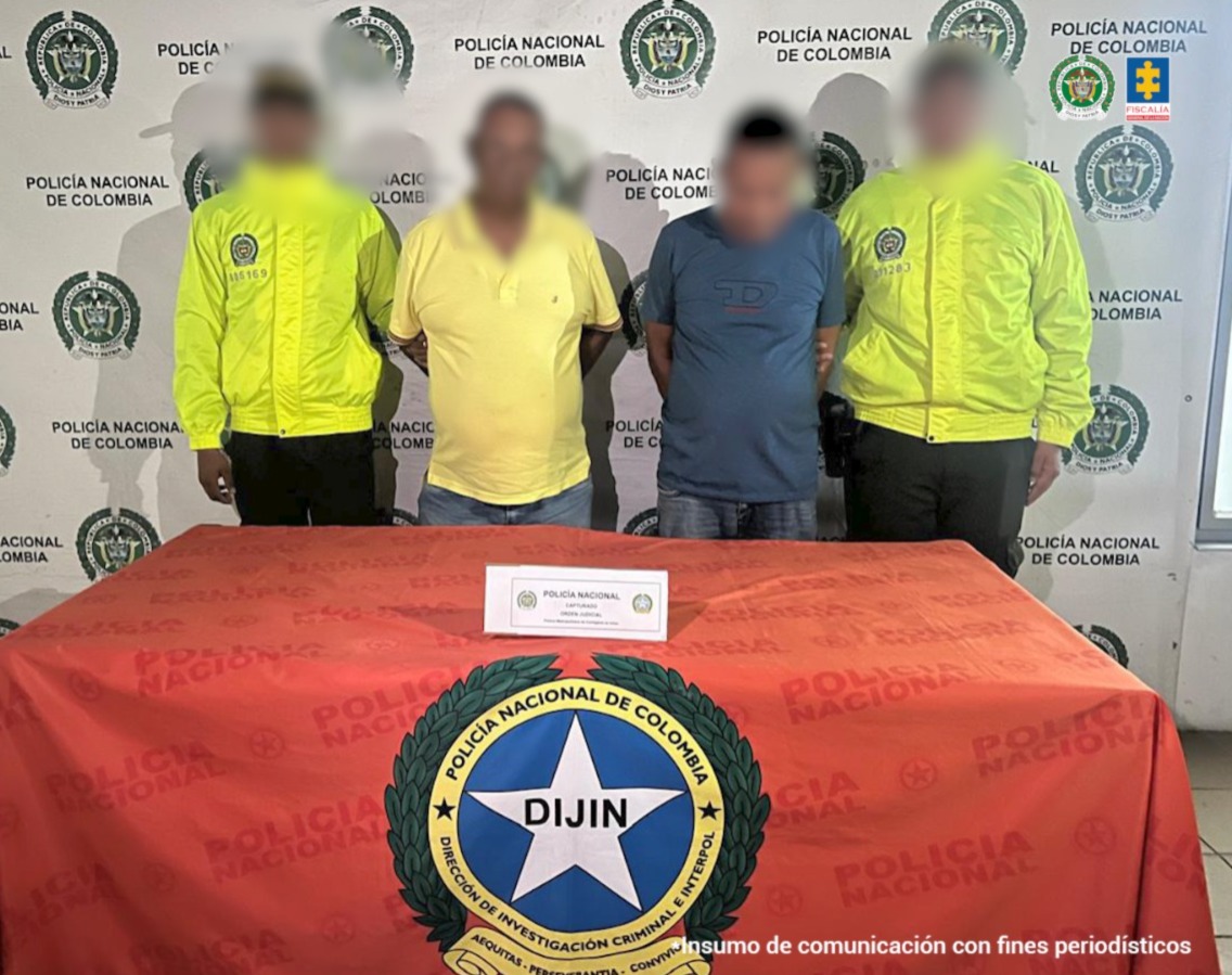 Texto alternativo: En la fotografía aparecen dos hombres de pie, con los brazos atrás esposados, uno tiene camiseta amarilla y el otro camiseta azul. Se encuentran custodiado por dos uniformados de la Policía Nacional.