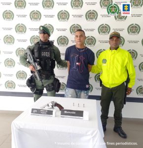 En la fotografía se observa a un hombre de camiseta azul con jean, custodiado por dos agentes de la Policía Nacional. Detrás de ellos se observa un pendón de esa institución.