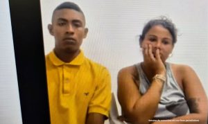 En la fotografía está un hombre moreno, delgado, joven, cabellos cortos negros, vestido con una camiseta amarilla. A su lado está una mujer trigueña, joven de cabellos negros recogidos, vestida con una camisilla gris. Ambos se encuentran al interior de una oficina asistiendo virtualmente a la audiencia en la que se le procesó.