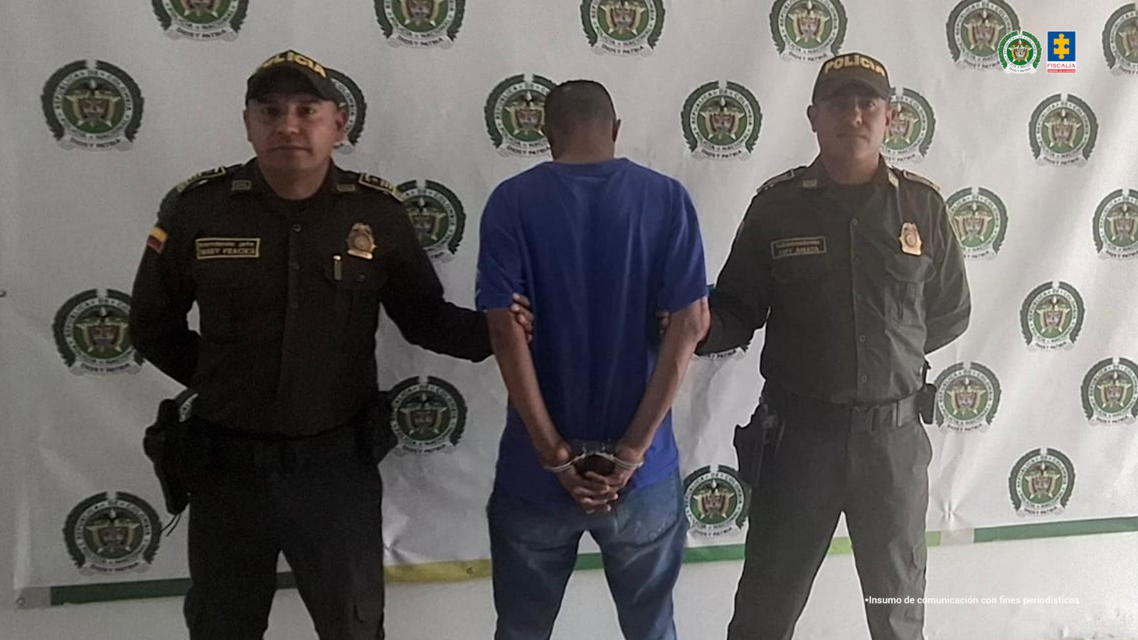 En la fotografía está un hombre de espalda con los brazos esposados, moreno, de cabellos negros cortos, vestido con camiseta y jean azul, custodiado por dos uniformados de la Policía Nacional.