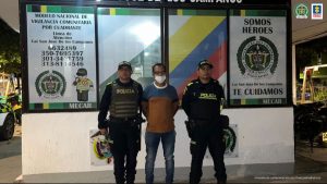 En la fotografía se observa a un hombre de camiseta azul con café y jean, custodiado por dos agentes de la Policía Nacional en una estación de policía.