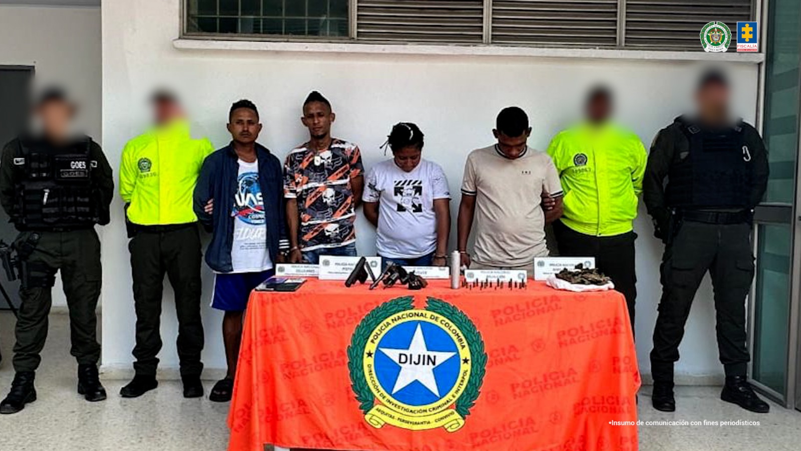 En la fotografía aparecen los procesados de pie con los brazos atrás esposado, custodiados por uniformados de la Policía Nacional. Delante de ellos hay una mesa donde están armas, municiones y droga incautada. 