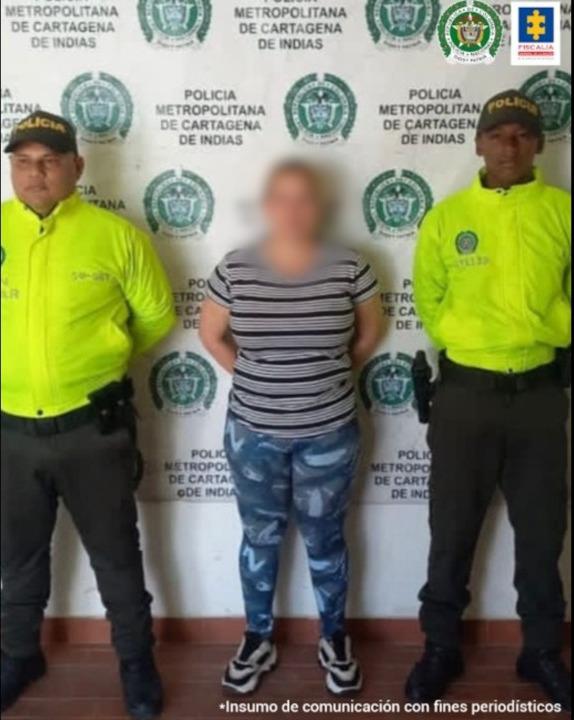 En la fotografía se observan tres personas, una de ellas la mujer capturada y dos uniformados de la Policía Nacioanl. En la parte posterior se observa un backing de con escudos de la Policía Nacional. 