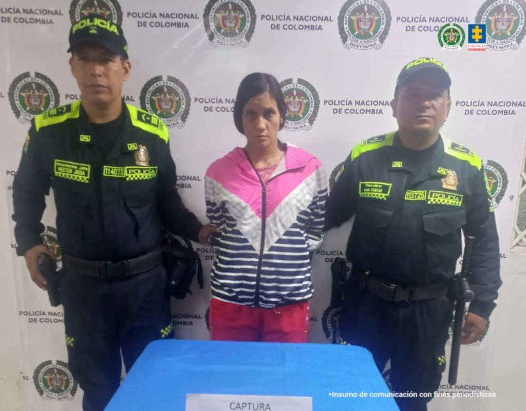 En la fotografía se aprecia de pie y con los brazos atrás a Stephani Cardona Pedroza. Viste con buso de cierre, con franjas anchas en forma de ‘V’ de colores fucsia y blanco, así como rayas horizontales azules y blancas; asimismo, usa pantalón rojo. A sus extremos hay uniformados de la Policía Nacional. Delante de ellos hay una superficie azul y sobre ella un letrero que dice: ‘Captura en flagrancia’. Detrás de ellos hay un pendón institucional de la Policía.