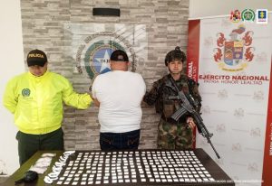 Fiscal Martha Mancera, Martha Mancera, Fiscal Mancera Se visualiza al capturado de espaldas junto a dos uniformados de la Policía y Ejército Nacional. Al frente una mesa con el material incautado. Detrás de ellos los banners institucionales de la Policía y Ejército Nacional.