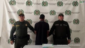 En la fotografía aparece de espaldas a la cámara Francisco Antonio Marquínez González. Viste con camisa de color negro, mangas cortas y ribetes blancos en las mangas y cuello; asimismo, pantalón negro. En los extremos hay uniformados de la Policía Nacional. Delante de ellos hay una superficie y sobre ella hay un letrero que dice: ‘Violencia intrafamiliar’. En la parte posterior hay un pendón institucional de la Policía.