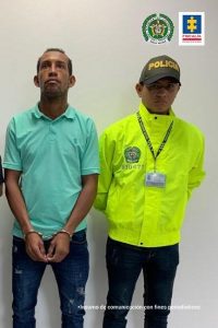 Hombre capturado y esposado. Se encuentra de pie y es acompañando a su izquierda por un funcionario de la SIJIN de la Policía Nacional.
