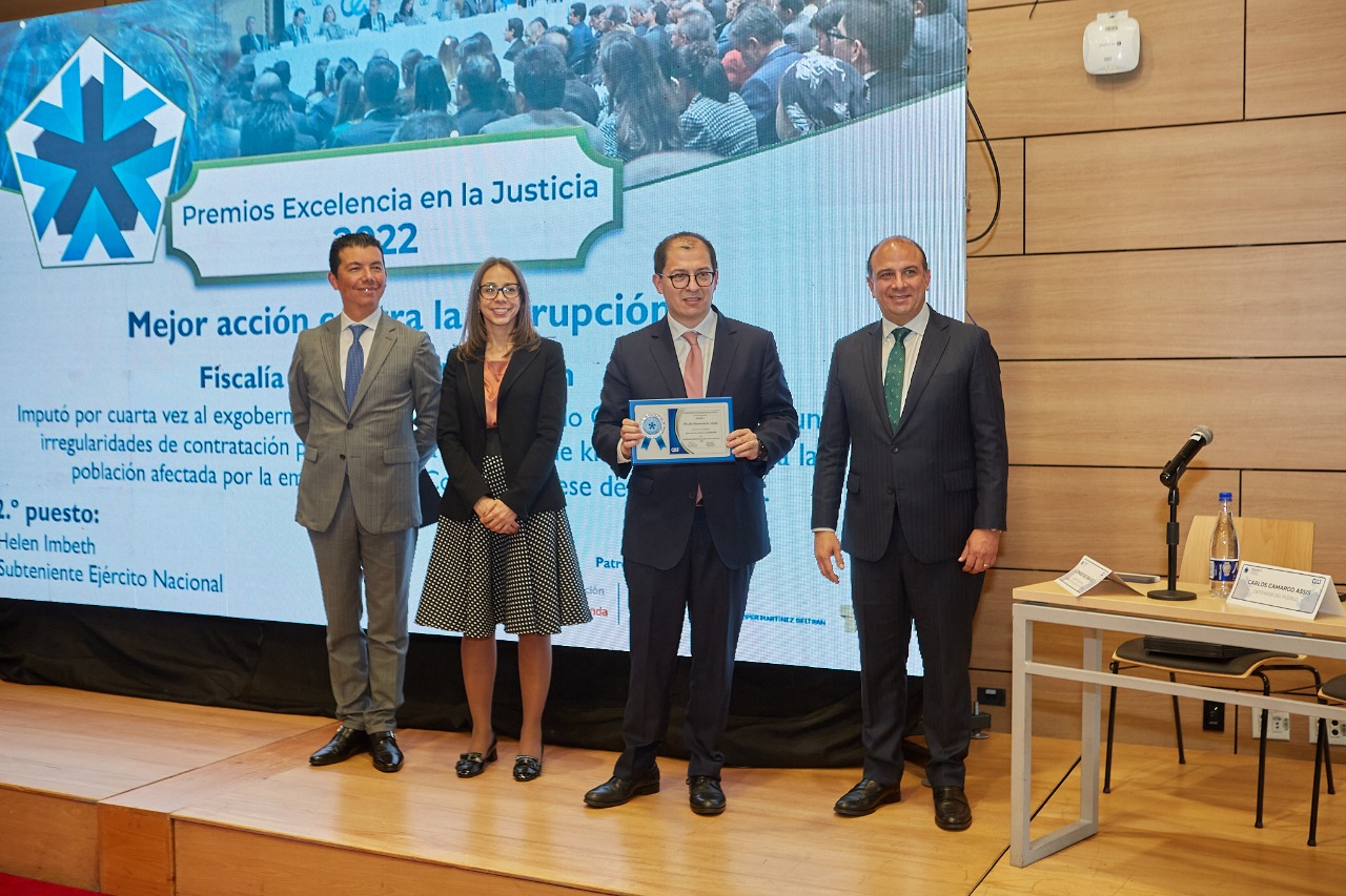 El Fiscal General de la Nación aparece junto al Defensor del Pueblo y dos personas más, sobre un escenario. 