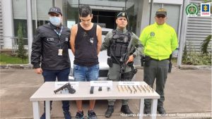 En la imagen se aprecia al capturado junto a un investigador del CTI y dos uniformados de la Policía Nacional. Al frente una mesa con un arma de fuego y munición incautada