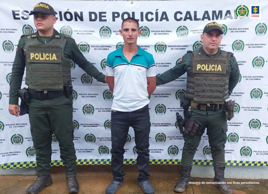 capturado y esposado con las manos atrás, custodiado por dos policías, detrás banner de la Policía Nacional.