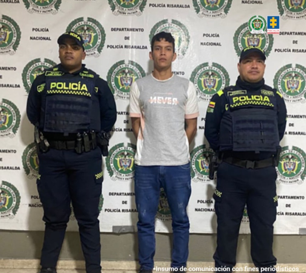 En la fotografía se aprecia de pie y con los brazos atrás a Freimar David Garzón Arcila. Viste camiseta de color gris con mangas cortas de color beage y ribetes color naranja claro; jean azul oscuro y zapatillas negras. A sus extremos hay uniformados de la Policía Nacional y detrás de ellos hay un pendón institucional de la Policía.