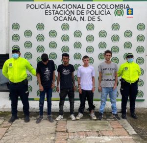 Se visualiza a los capturados junto a dos uniformados de la Policía Nacional. Detrás de ellos el banner que identifica a la Policía Nacional en Ocaña (Norte de Santander