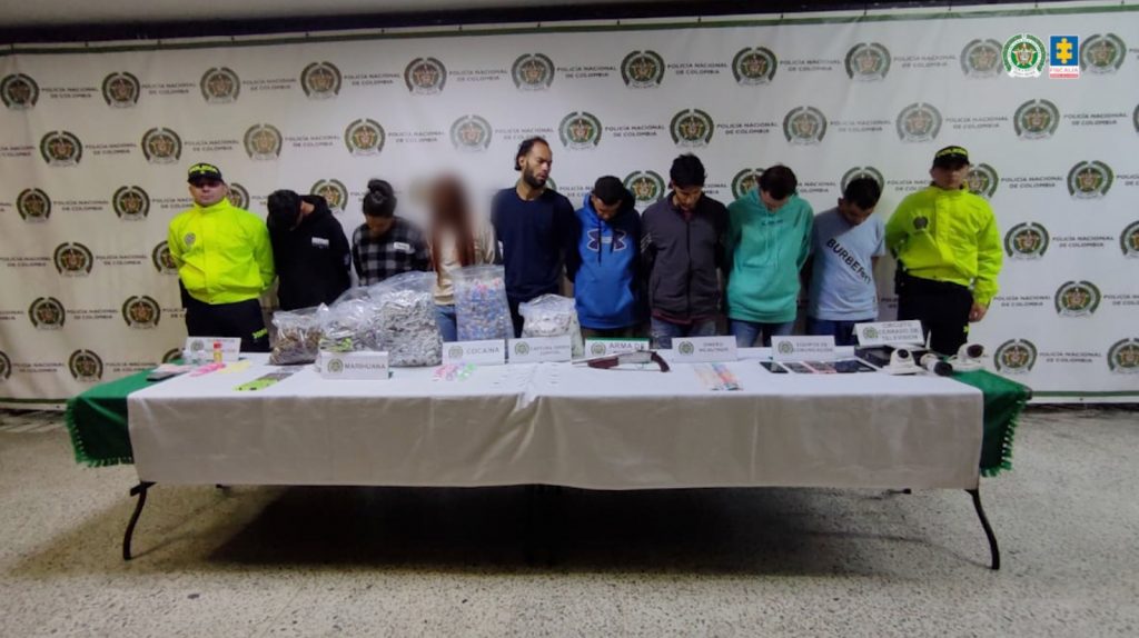 En la imagen están los procesados en medio de dos servidores de la Policía Nacional y una mesa adelante con la droga y demás elementos incautados.