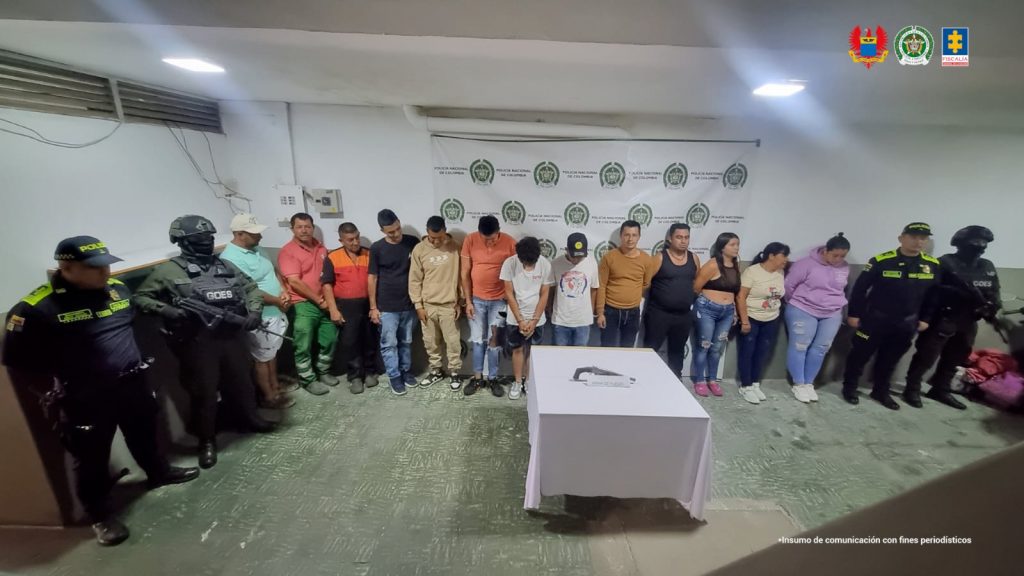 En la imagen se ve un grupo de personas detenidas bajo custodia de integrantes de la Policía Nacional.