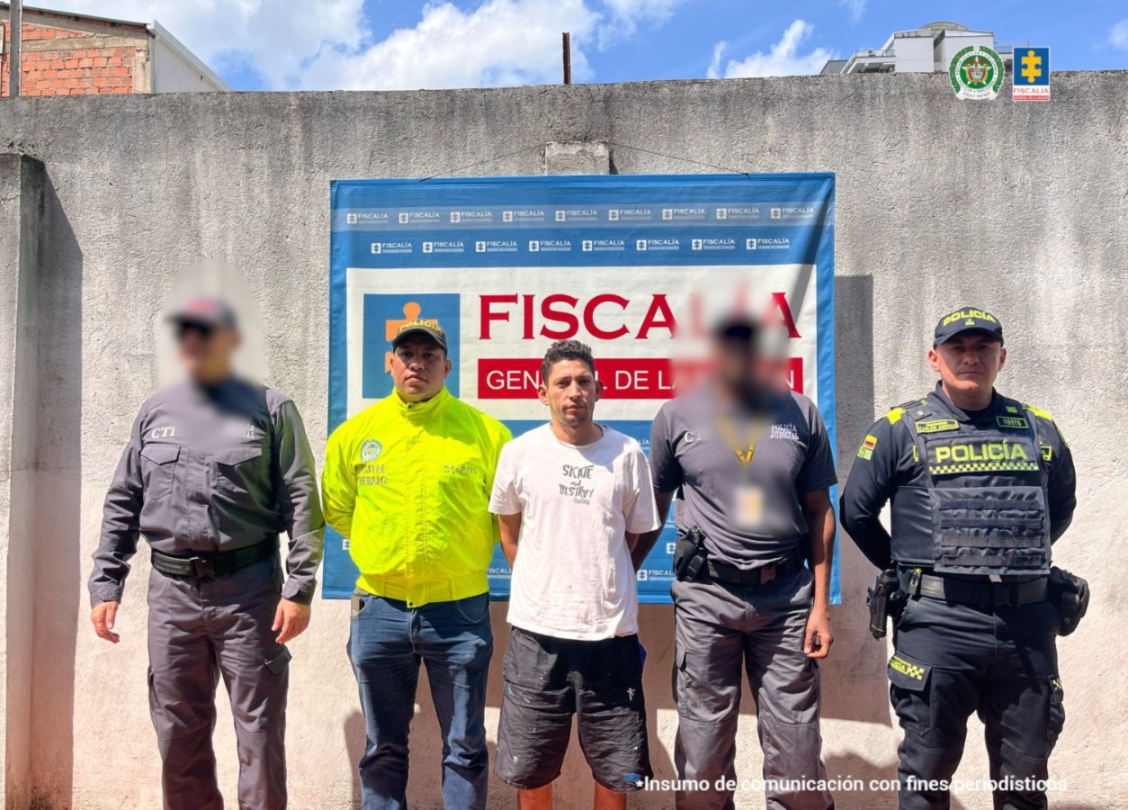 El capturado aparece de pie, en el centro de la imagen, con las manos esposadas en la espalda. Está rodeado de miembros del CTI de la Fiscalía y de la Policía.