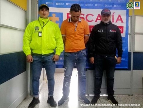 En la fotografía se observa al capturado junto a un investigador del CTI y un funcionario de la SIJIN. En la parte posterior se aprecia el banner que identifica a la Fiscalía General de la Nación