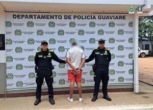  capturado de espaldas custodiado por dos policías. Detrás banner de la Policía Nacional.