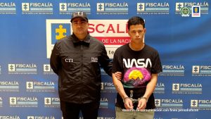 En la imagen está el presunto responsable del homicidio de un químico, acompañado de un servidor del CTI y un pendón azul de la Fiscalía General de la Nación al fondo