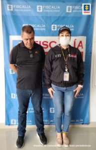 En la foto aparece de pie y con los brazos atrás, Gildardo Antonio Gallo Serna. Viste camisa negra de manga corta, jean azul y zapatillas negras. A su izquierda hay una servidora del CTI de la Fiscalía. Detrás de ellos hay un pendón institucional de la Fiscalía.