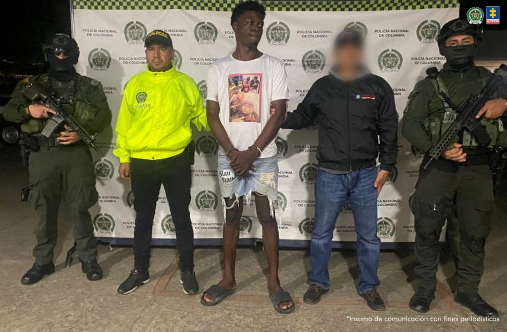 En la fotografía aparecen los dos capturados junto a dos servidores del CTI y tres agentes de la Policía. En la parte superior están un banner de la Fiscalía General de la Nación y otro banner de la Policía Nacional