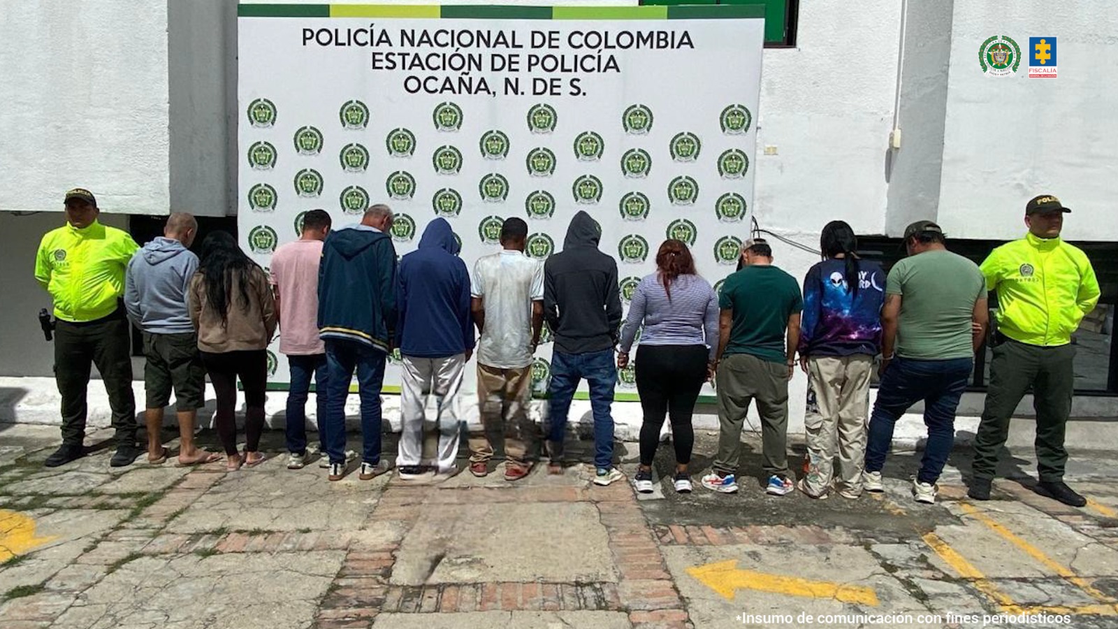 Se visualiza a los 12 capturados de espaldas junto a dos uniformados de la Policía Nacional. Detrás de ellos el banner que identifica a Estación de Policía de Ocaña (Norte de Santander)