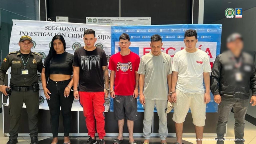 Se visualiza a los capturados junto a un investigador del CTI y un uniformado de la Policía Nacional. Detrás de ellos os banner que identifican a la Policía Nacional y Fiscalía General de la Nación.