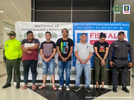 En la fotografía se aprecian los cinco capturados junto a uniformados de la Policía Nacional. En la parte posterior se observan los banners que identifican a la Policía Nacional y al CTI de la Fiscalía General de la Nación.