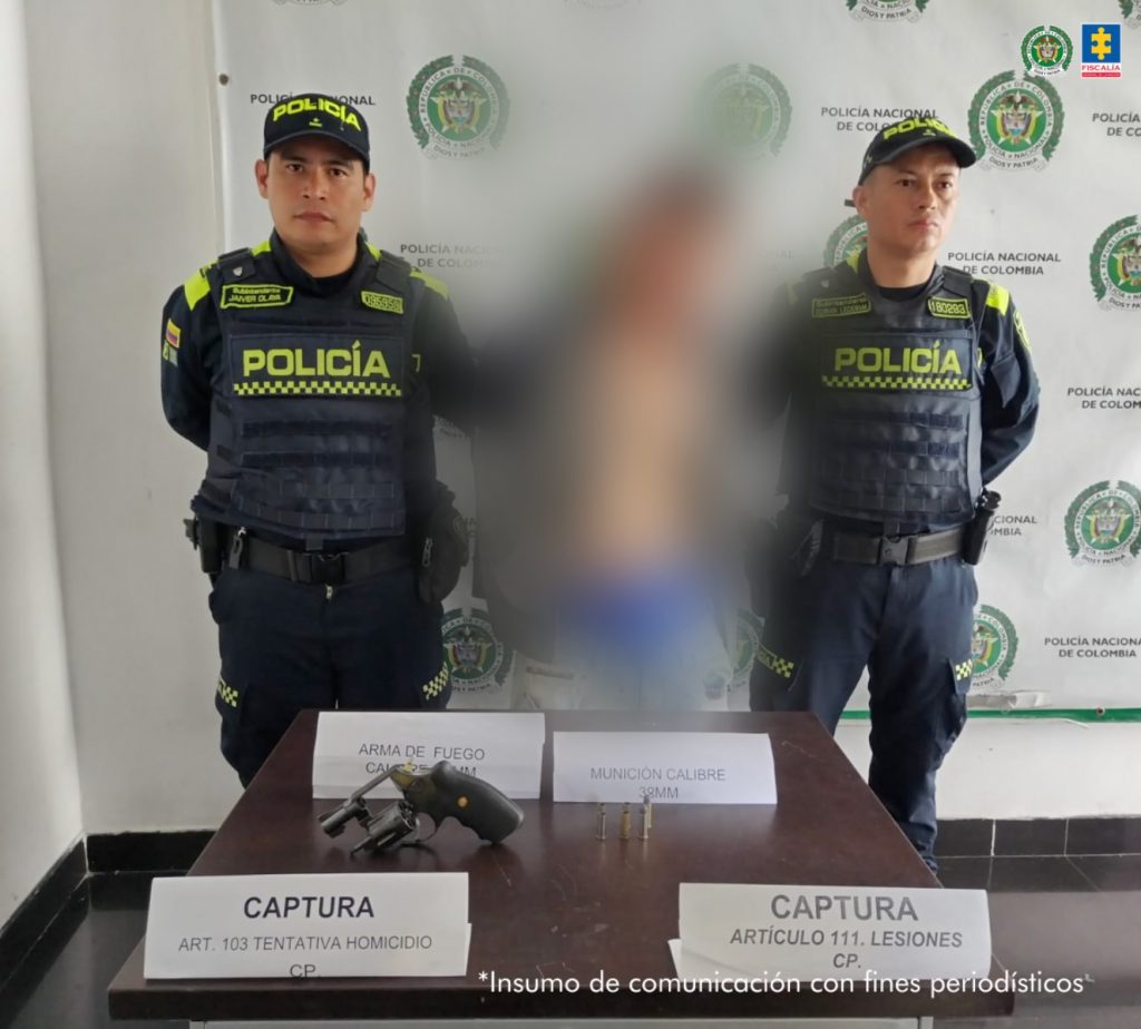 Se observa al capturado de frente y con un efecto de blurr que le cubre el cuerpo y el rostro. A cada costado un funcionario de la Policía Nacional.