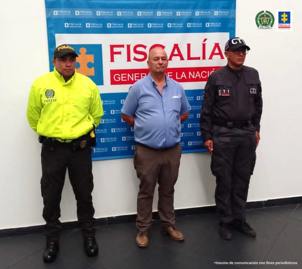 Se observa al capturado de frente a un lado un funcionario del CTI y al otro uno de Policía Nacional. Atrás un pendón de Fiscalía
