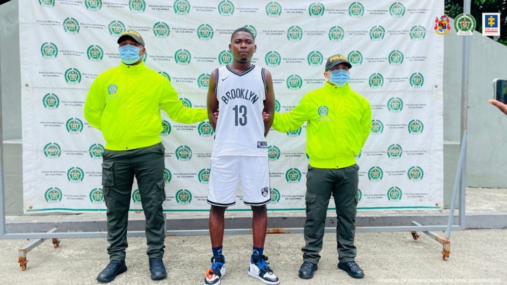 Harry Murillo Andrade, alias Soldado o Soldadito aparece en la foto con dos policías a sus lados y un backing con logos de la Policia Nacional en la parte de atrás.