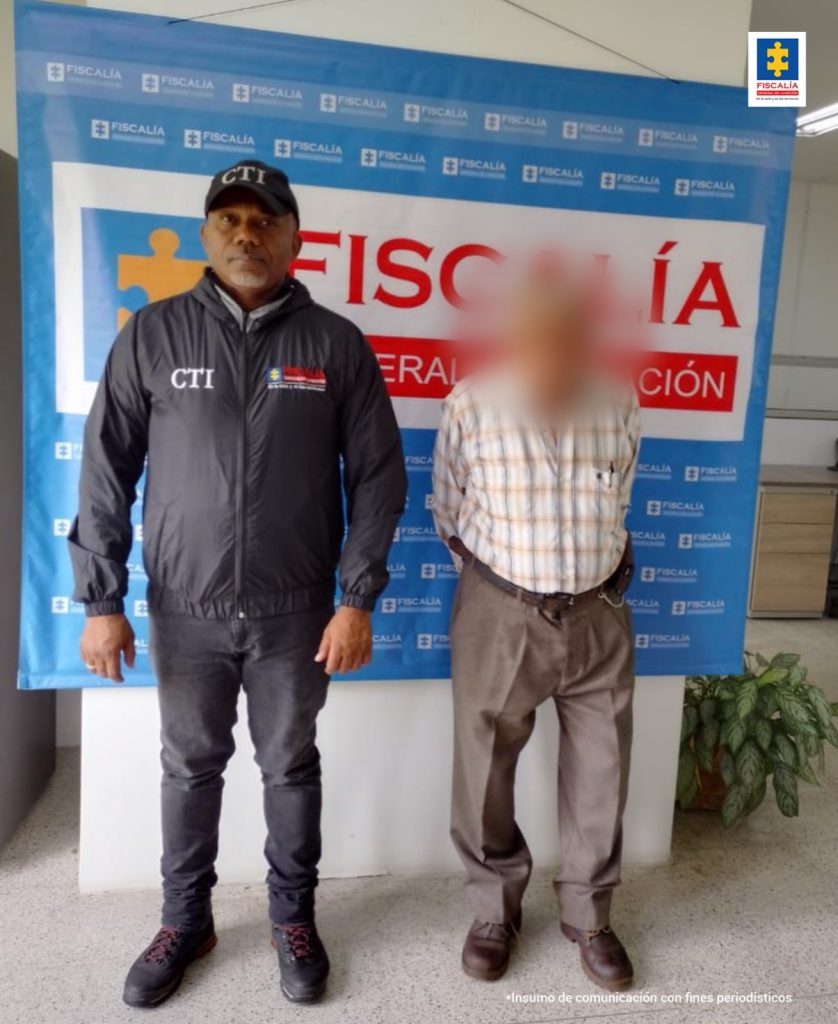 En la imagen está el hombre de 79 años custodiado por un servidor del CTI y detrás un pendón azul de la Fiscalía General de la Nación.