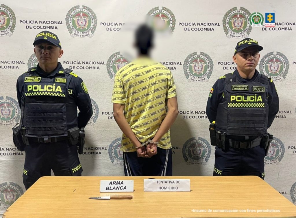 Se observa al capturado de espaldas y custodiado por dos funcionarios de Policía Nacional. Atrás, un pendón de Policía Nacional.