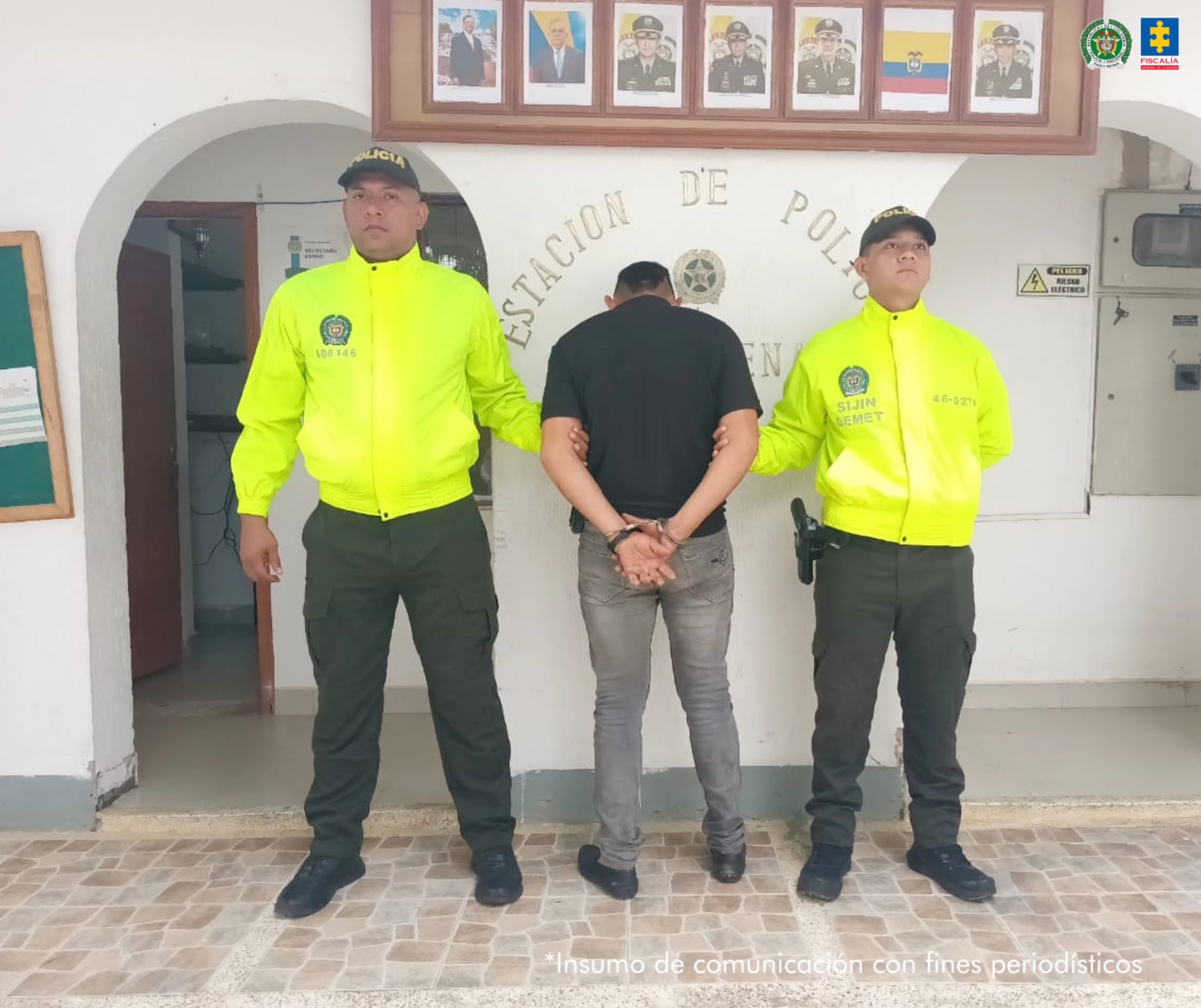 capturado de espaldas custodiado por dos policías. Detrás banner de la Policía Nacional.