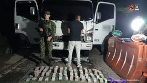 El imputado se encuentra en custodia por un uniformado del Ejército Nacional y se observa el camión donde transportaba el dinero incautado.