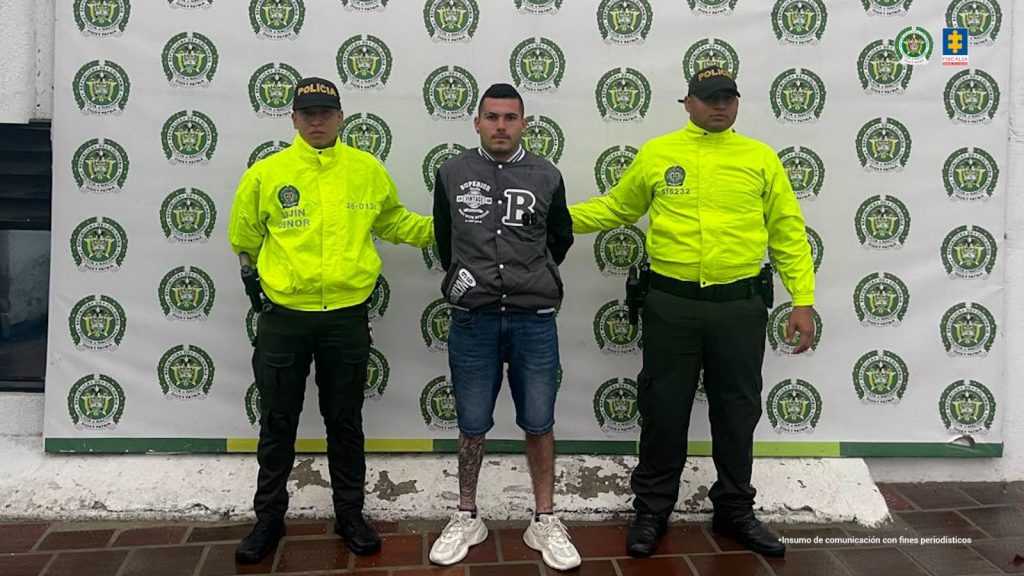 Se visualiza al capturado junto a uniformados de la Policía Nacional. Detrás de ellos el banner que identifica a la Policía Nacional