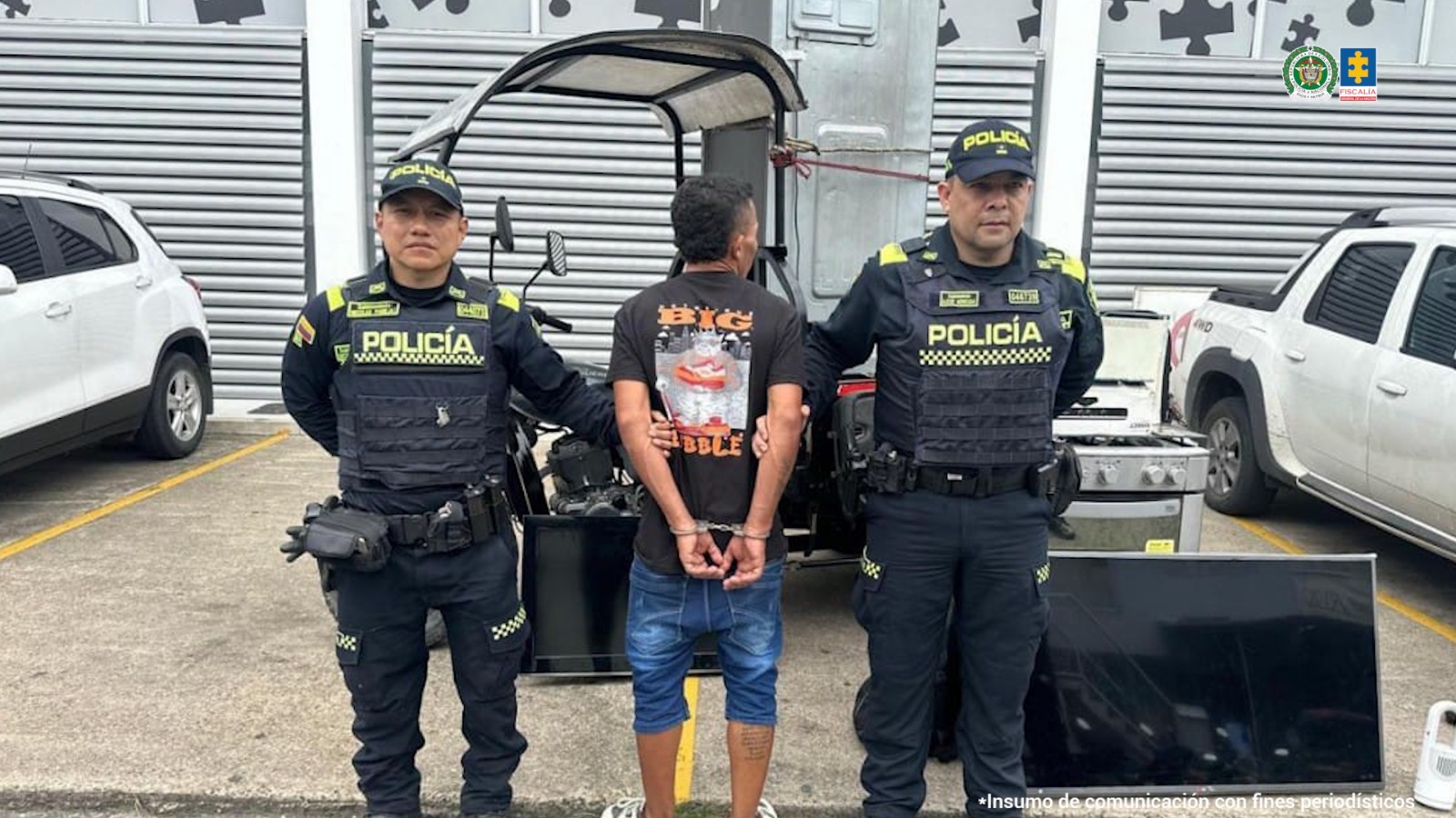 El capturado aparece de espaldas rodeado de dos miembros de la Policía. En la parte trasera de la imagen pueden verse algunos vehículos. 