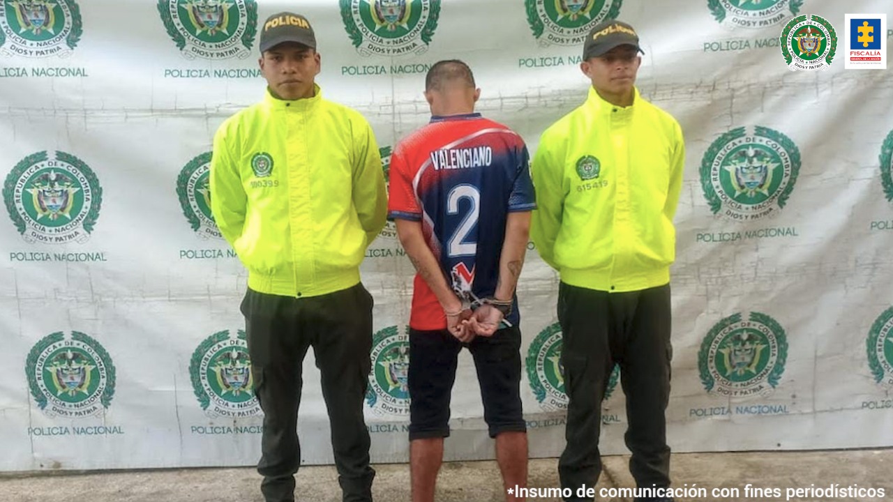 El hombre está esposado con sus manos, le da la espalda a la cámara y está protegido por dos miembros de la Policía Nacional.