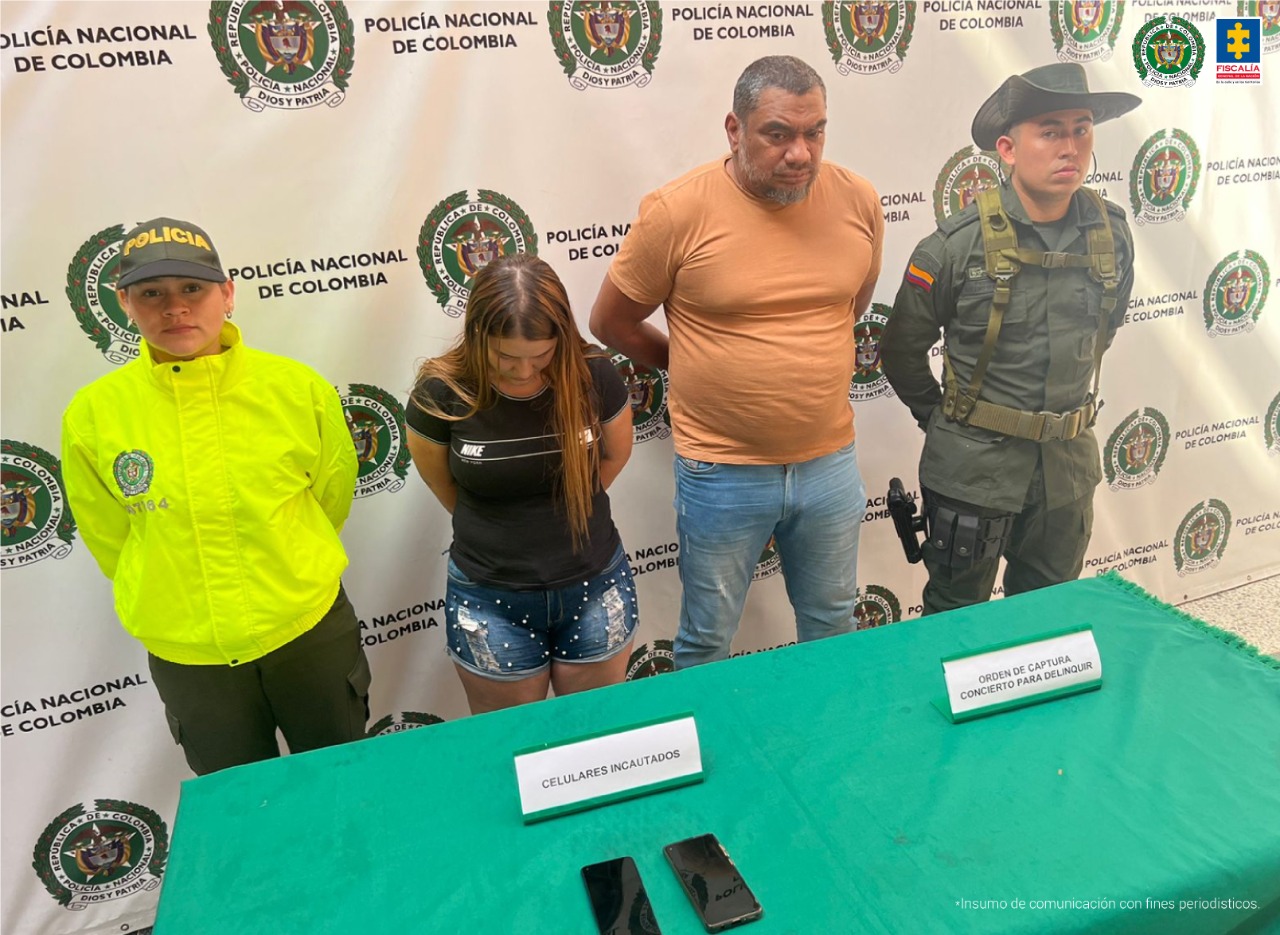 Dos personas capturadas, un hombre y una mujer, aparecen parados en medio de personal de la Policía Nacional.